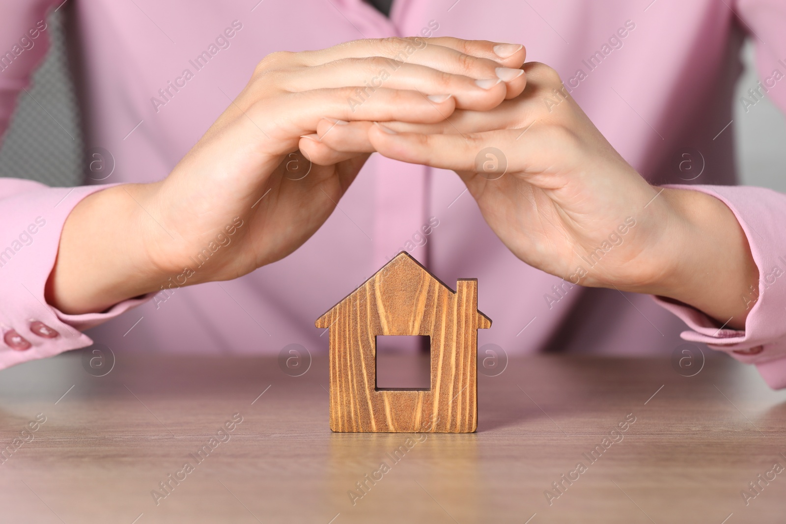 Photo of Property insurance. Real estate agent protecting wooden house figure at table indoors, closeup