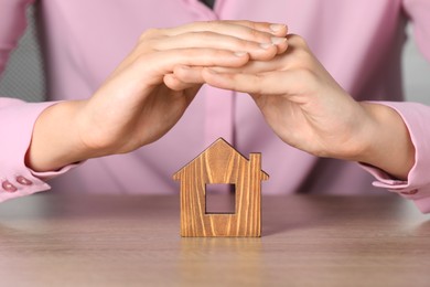 Photo of Property insurance. Real estate agent protecting wooden house figure at table indoors, closeup