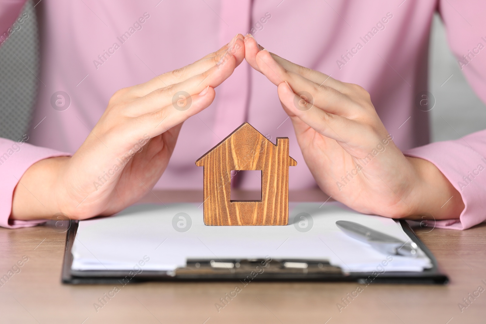 Photo of Property insurance. Real estate agent protecting wooden house figure at table indoors, closeup