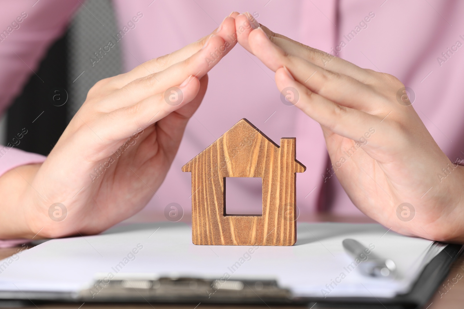 Photo of Property insurance. Real estate agent protecting wooden house figure at table indoors, closeup