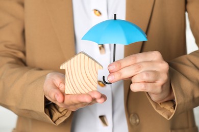 Photo of Property insurance. Real estate agent holding small umbrella above wooden house figure, closeup