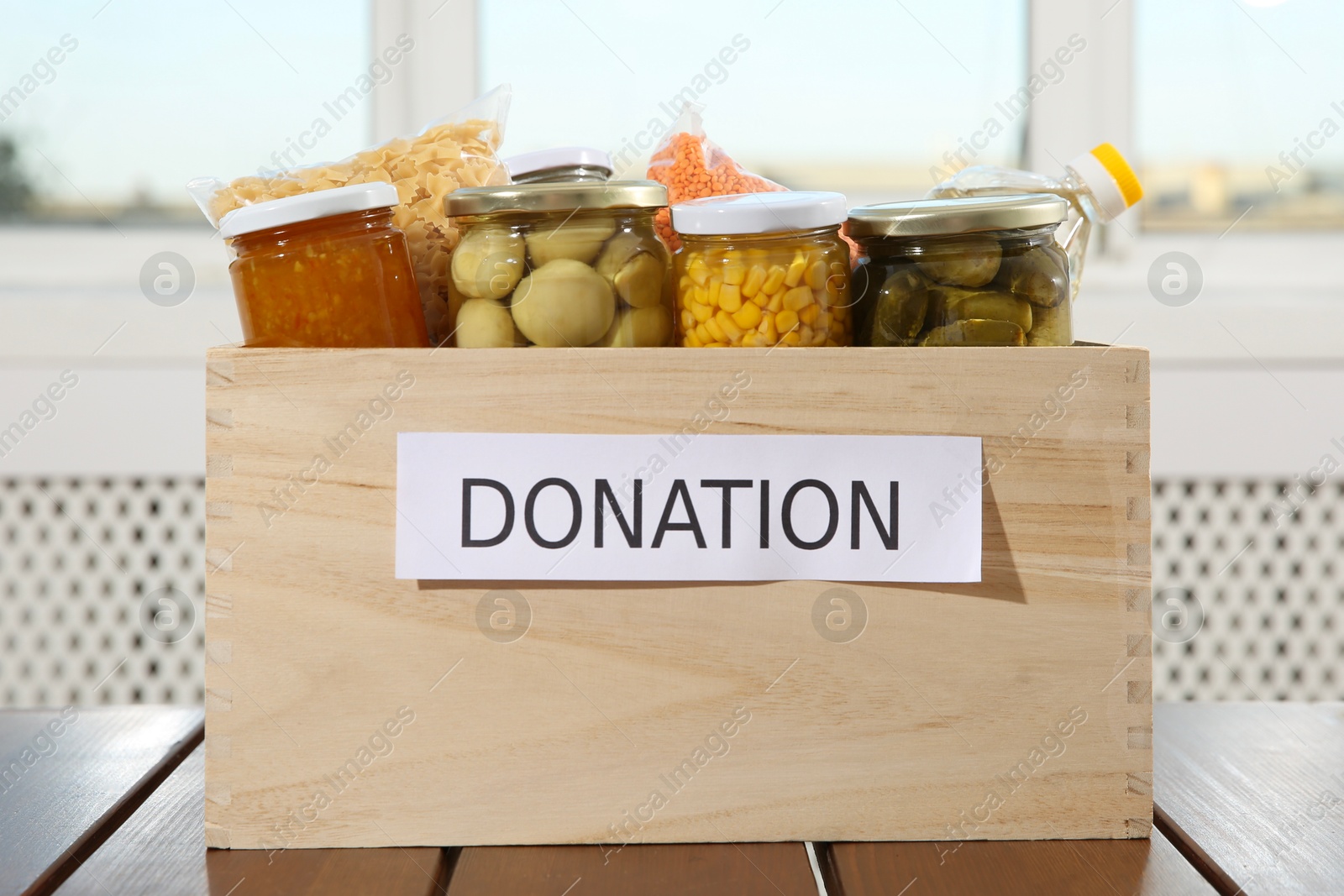 Photo of Different food products for donation in crate on wooden table indoors