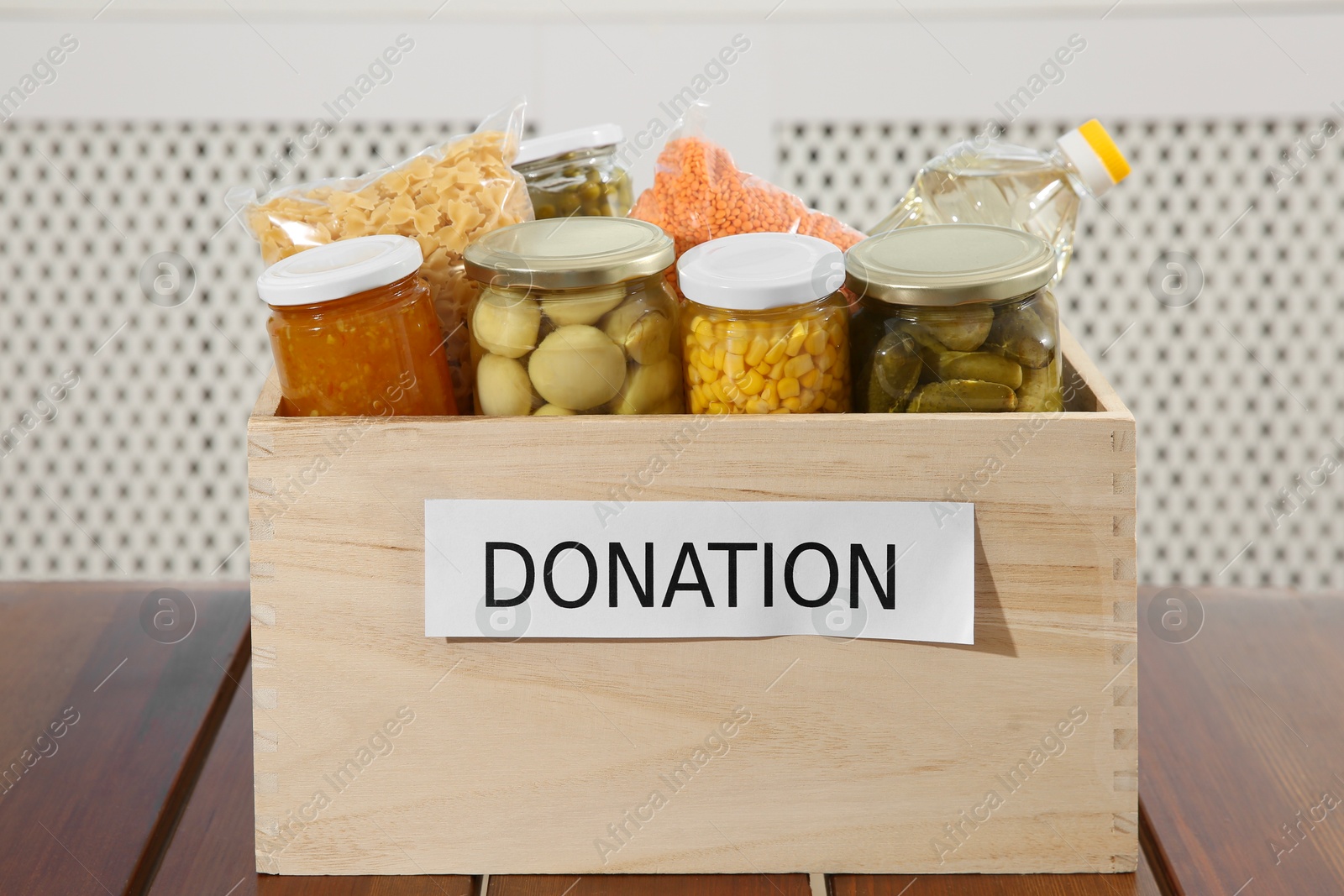 Photo of Different food products for donation in crate on wooden table indoors