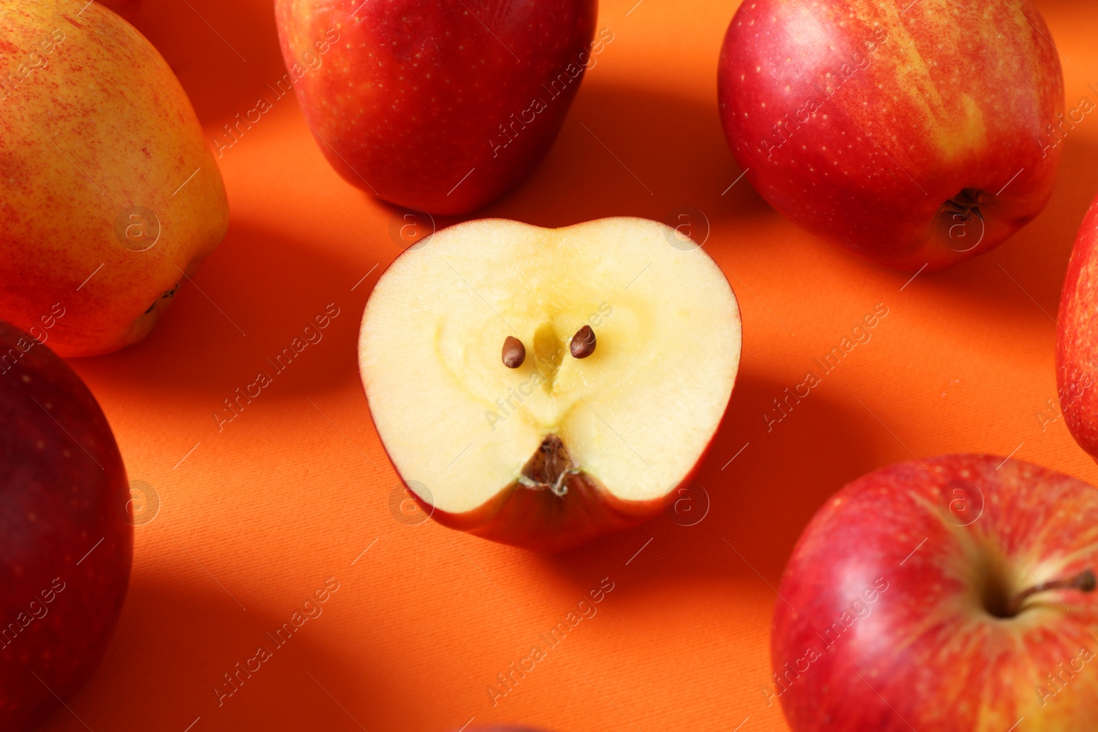 Photo of Whole and cut fresh red apples on orange background, closeup