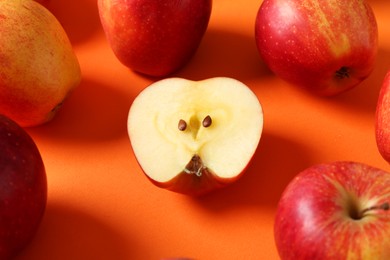 Whole and cut fresh red apples on orange background, closeup