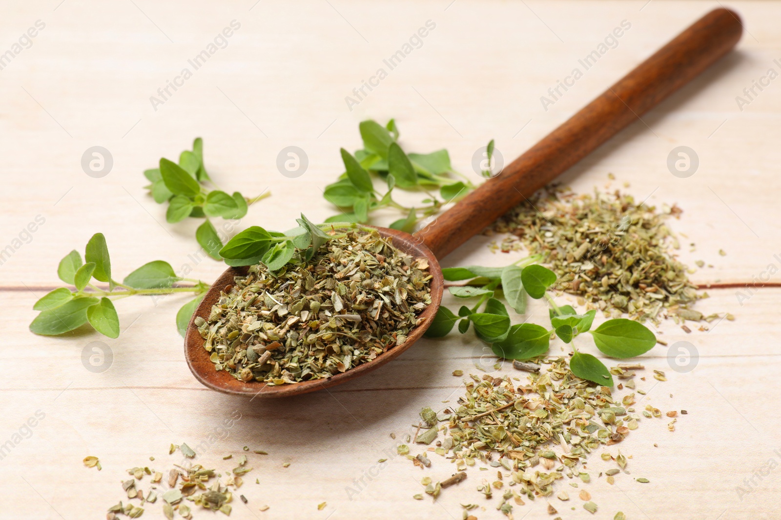 Photo of Dried oregano in spoon and green leaves on wooden table