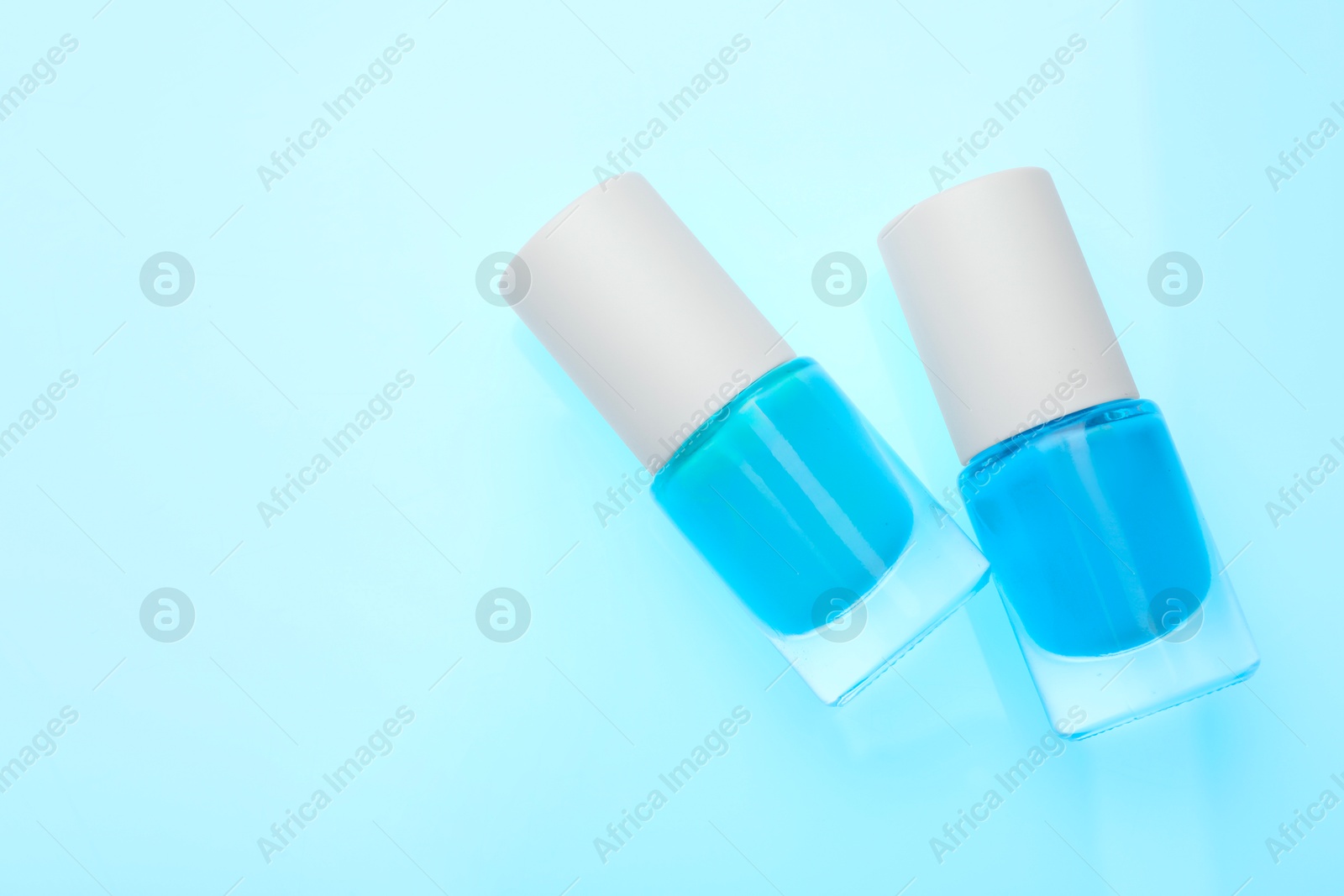 Photo of Nail polish in bottles on light blue background, top view. Space for text