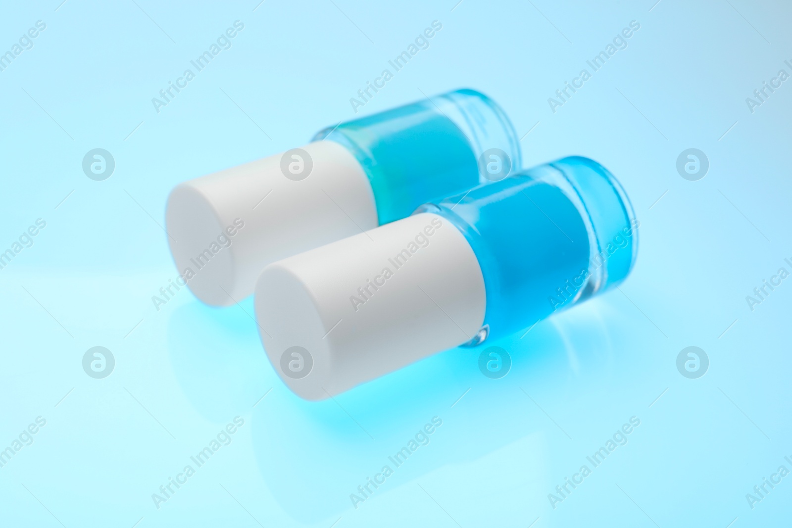 Photo of Nail polish in bottles on light blue background, closeup