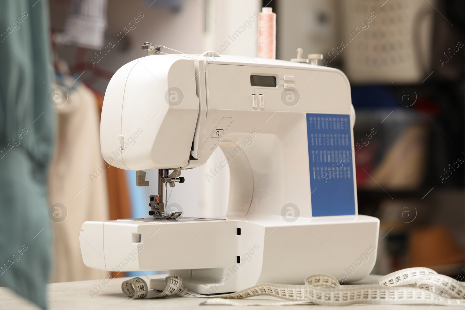 Photo of One sewing machine with thread and measuring tape on white table in workshop