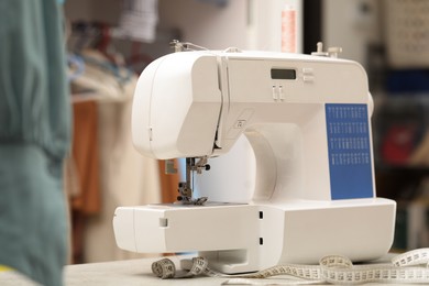 Photo of One sewing machine with thread and measuring tape on white table in workshop