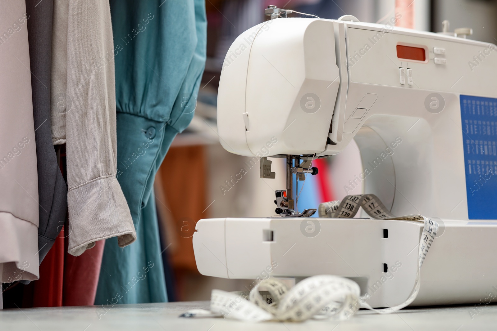 Photo of One sewing machine with thread and measuring tape on white table in workshop