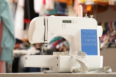 Photo of One sewing machine with thread and measuring tape on table in workshop