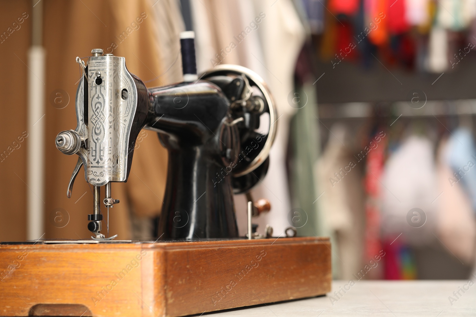 Photo of Vintage sewing machine with thread on table in workshop, closeup. Space for text