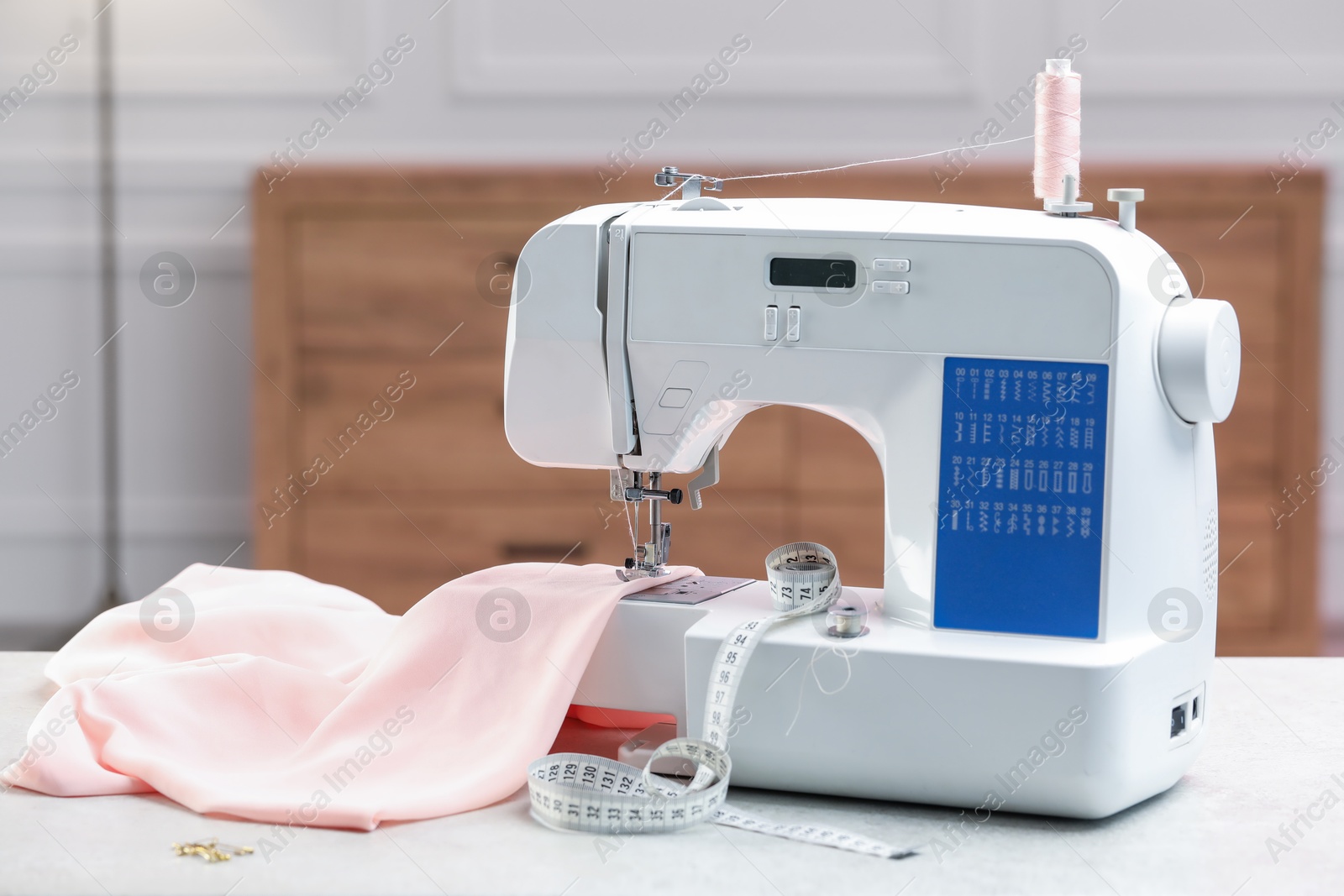 Photo of Sewing machine with threads, measuring tape and fabric on white table in workshop