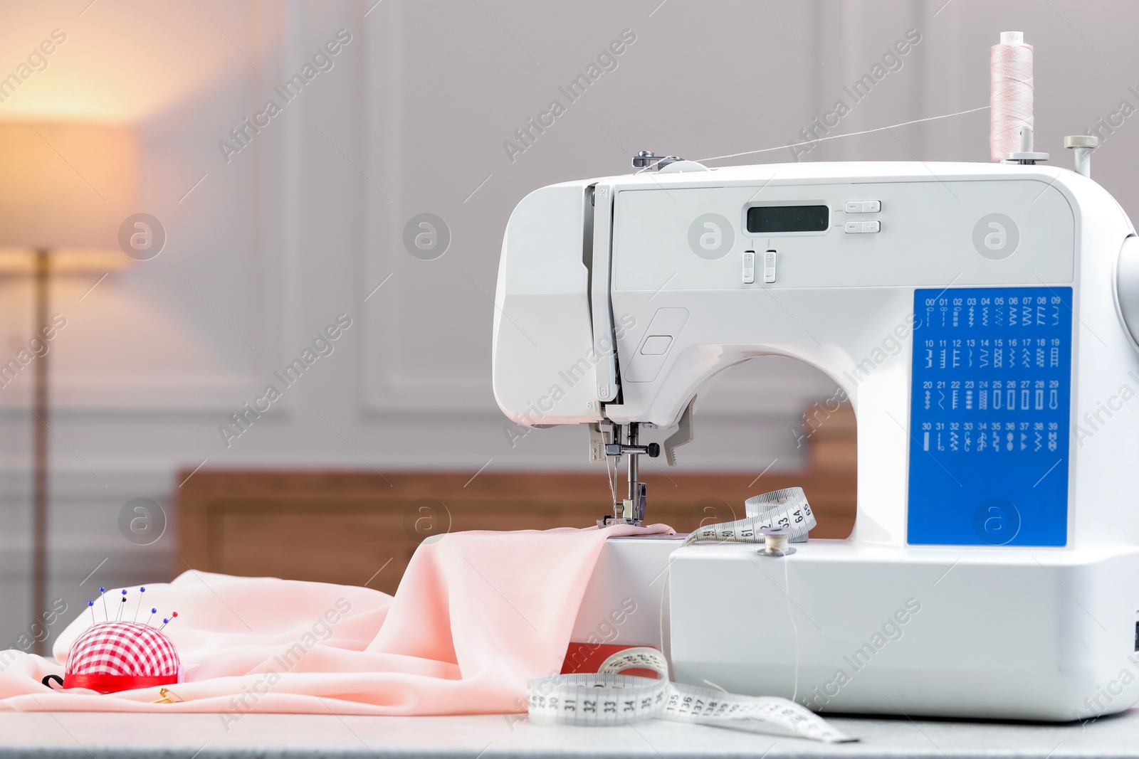 Photo of Sewing machine with fabric and other supplies on white table in workshop, space for text