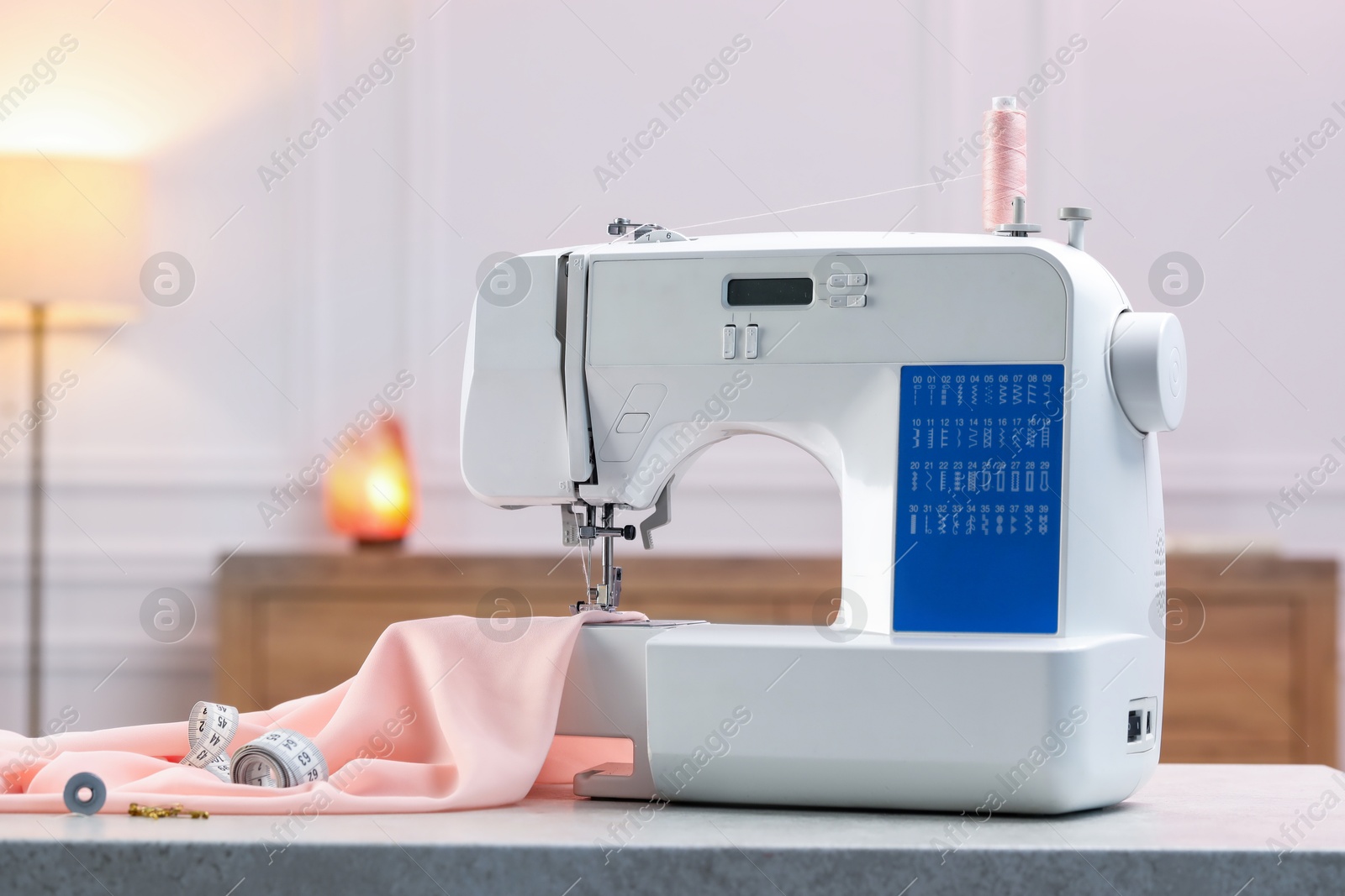 Photo of Sewing machine with threads, measuring tape and fabric on white table in workshop