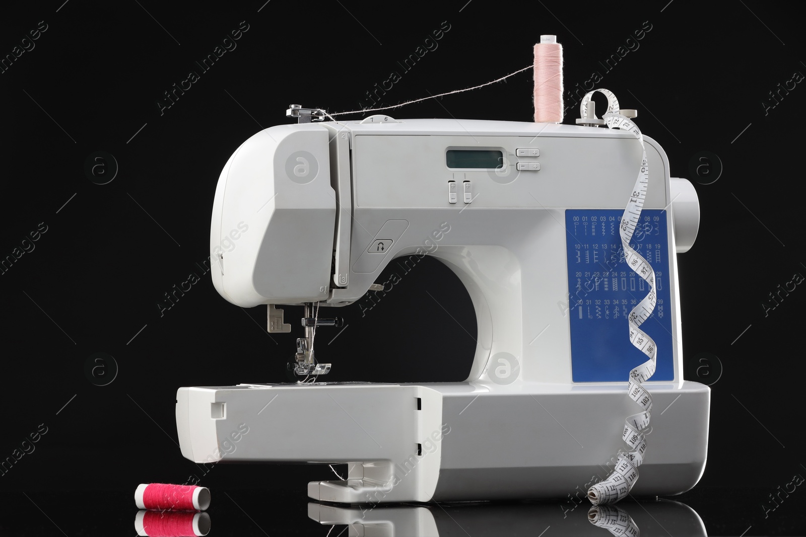 Photo of Sewing machine with measuring tape and spools of threads on black background