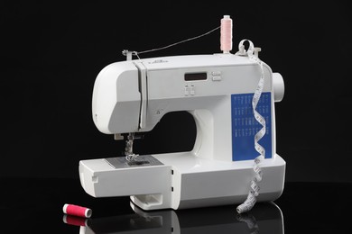 Photo of Sewing machine with measuring tape and spools of threads on black background