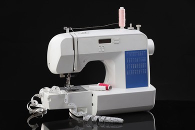 Photo of Sewing machine with measuring tape and spools of threads on black background