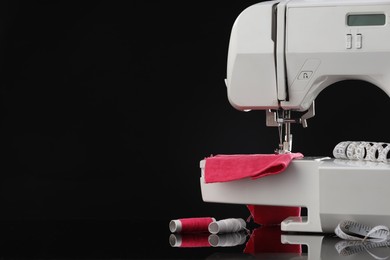 Photo of Sewing machine with measuring tape, fabric and spools of threads on black background, space for text