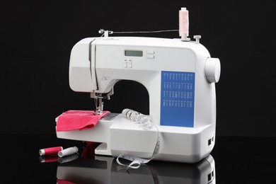 Photo of Sewing machine with measuring tape, fabric and spools of threads on black background