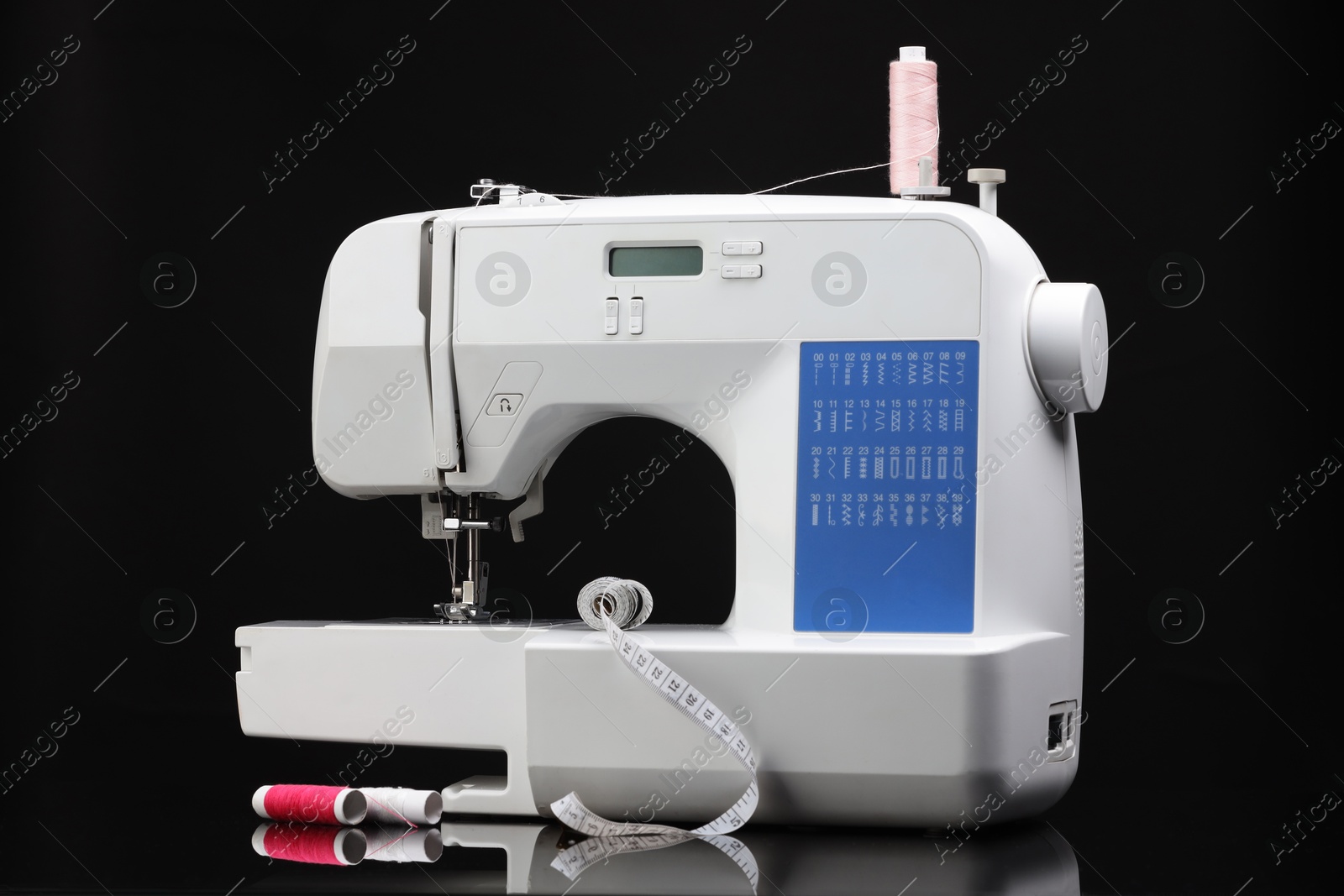 Photo of Sewing machine with measuring tape and spools of threads on black background