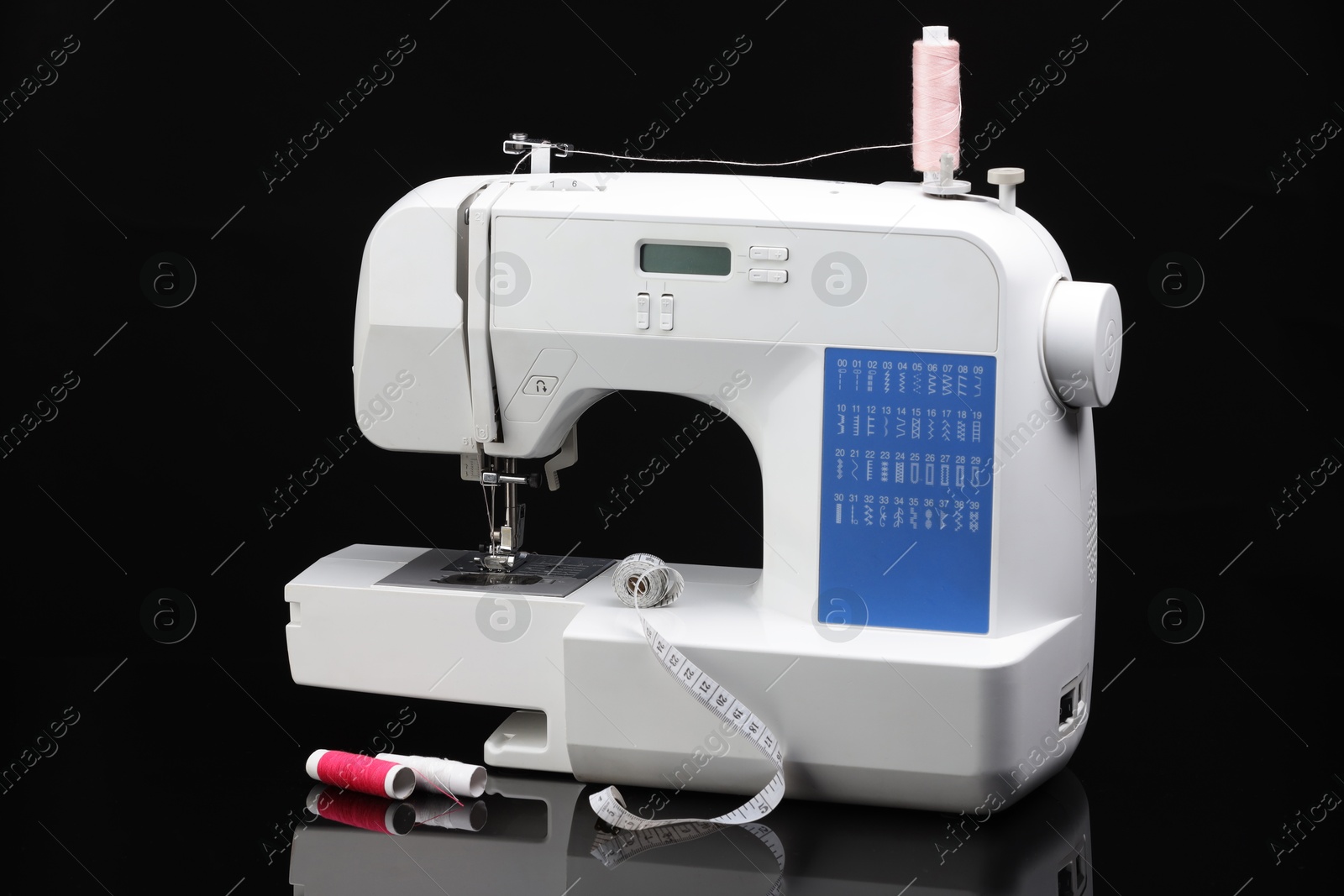 Photo of Sewing machine with measuring tape and spools of threads on black background