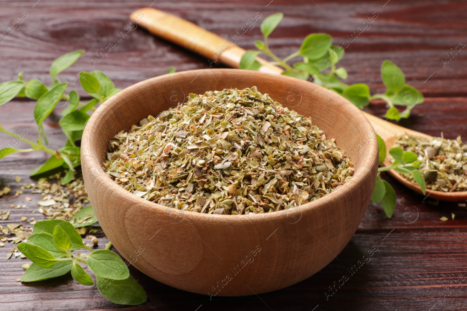 Photo of Dried oregano in bowl, spoon and green leaves on wooden table, closeup