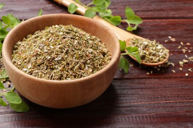 Photo of Dried oregano in bowl, spoon and green leaves on wooden table, closeup