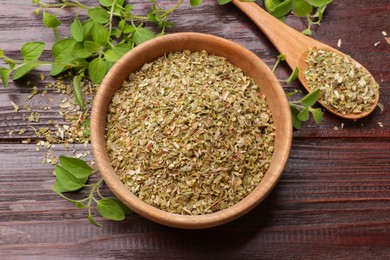 Photo of Dried oregano in bowl, spoon and green leaves on wooden table, top view