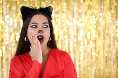 Photo of Emotional woman with cat makeup and ears on golden background. Space for text