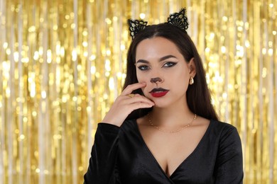 Photo of Beautiful woman with cat makeup and ears on golden background