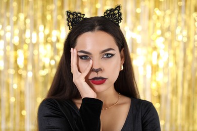 Photo of Beautiful woman with cat makeup and ears on golden background