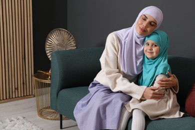 Photo of Muslim woman and her daughter sitting on sofa at home, space for text