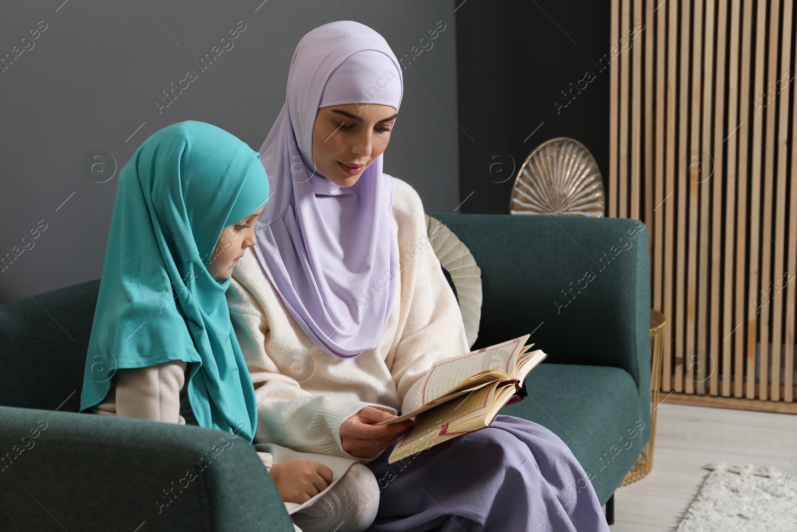 Photo of Muslim woman and her daughter reading Quran at home