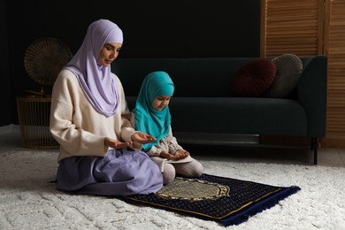 Photo of Muslim woman and her daughter praying on mat at home, space for text