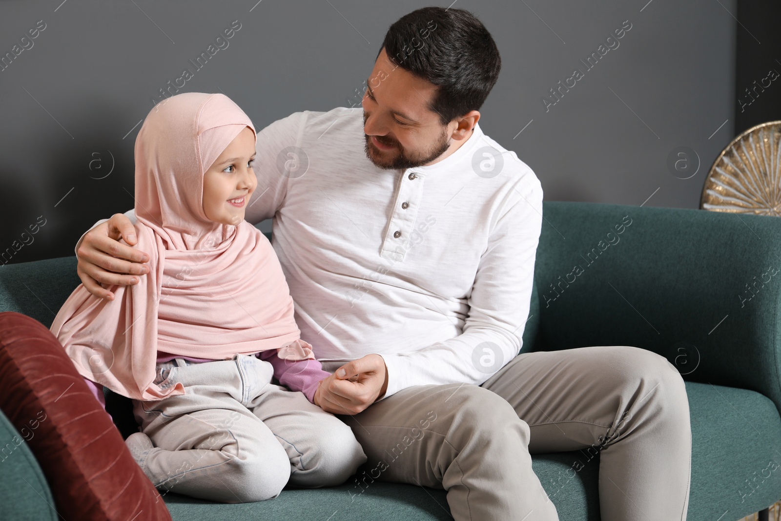 Photo of Muslim man and his daughter sitting on sofa at home