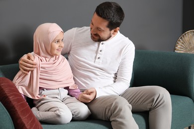 Photo of Muslim man and his daughter sitting on sofa at home