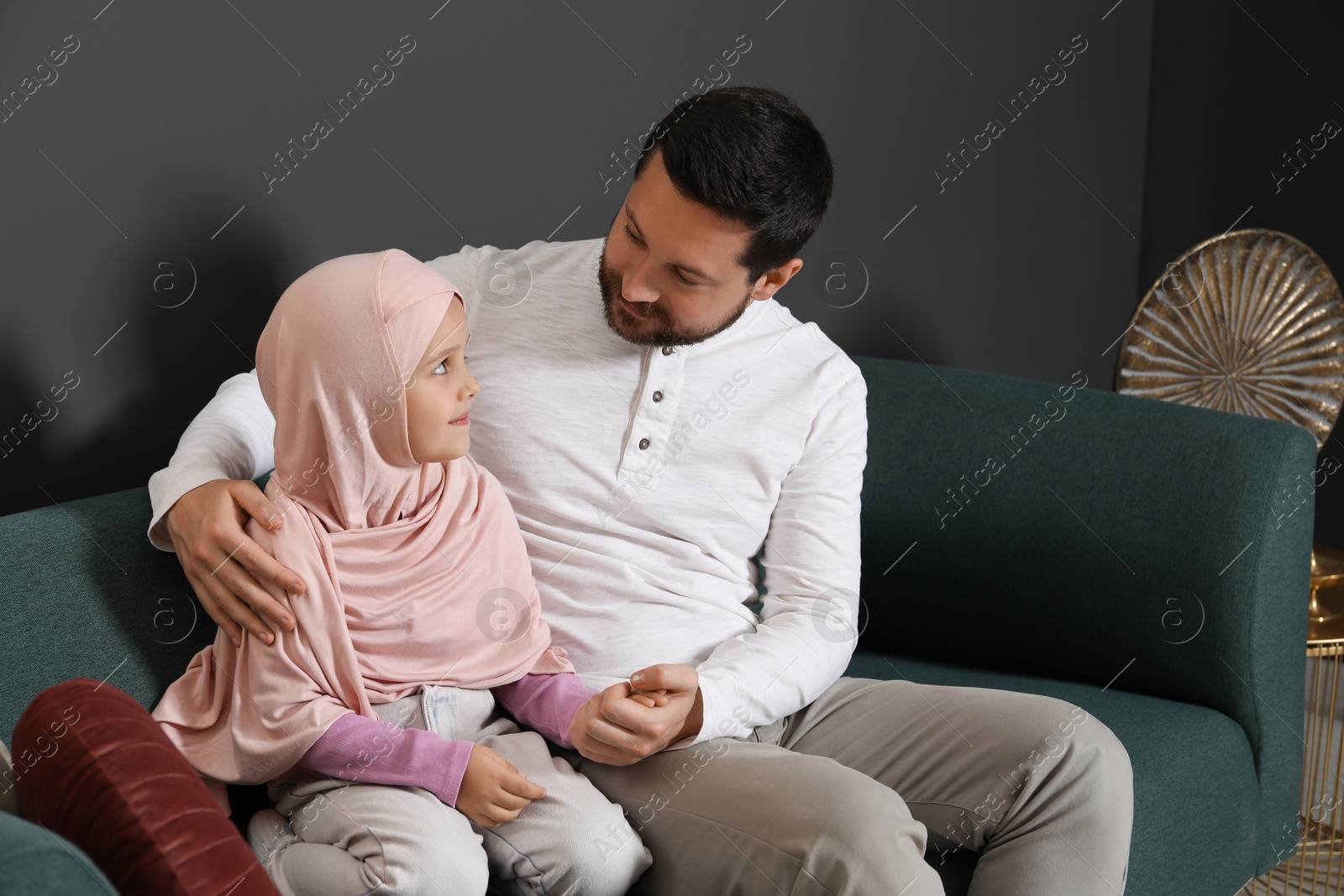 Photo of Muslim man and his daughter sitting on sofa at home