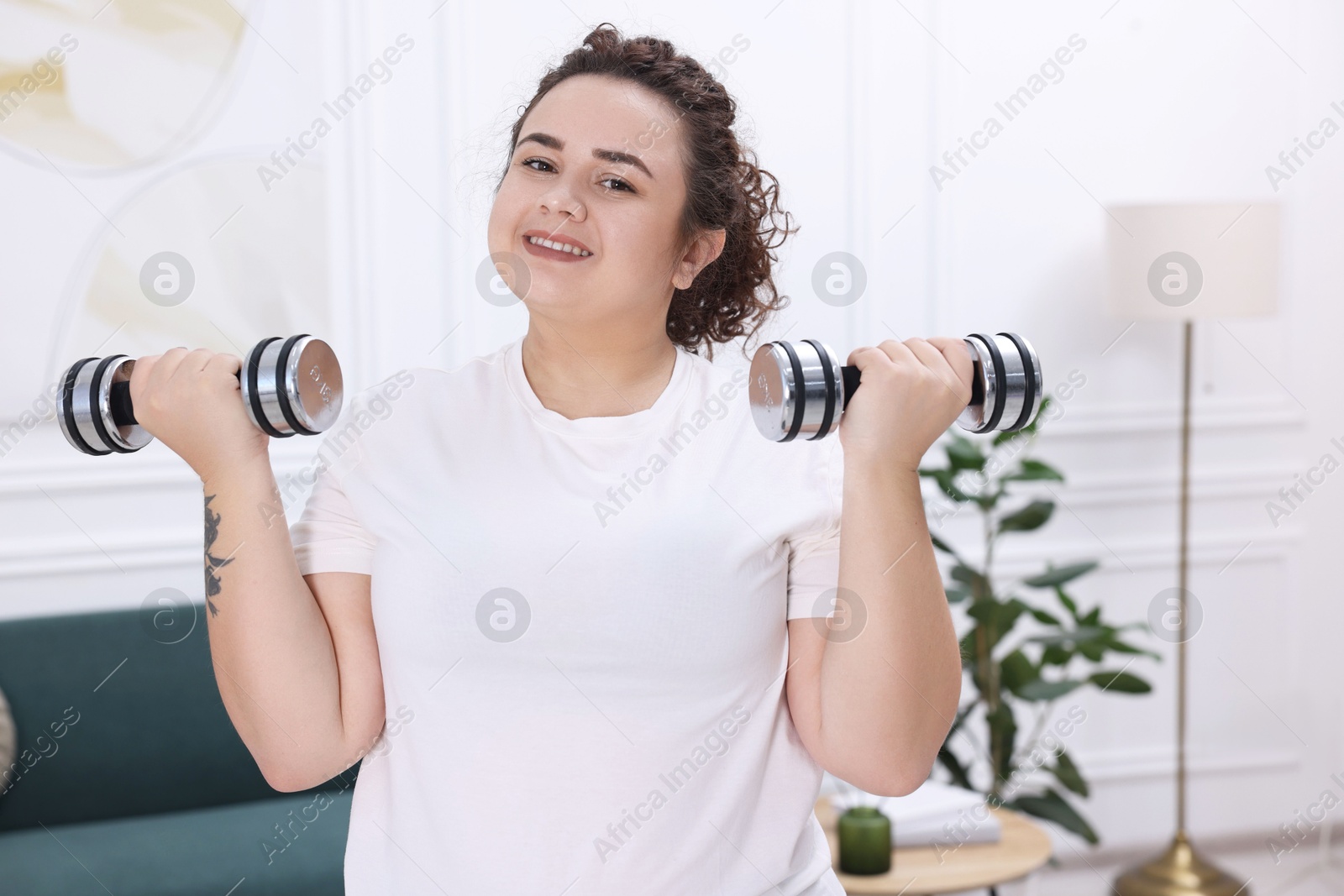 Photo of Plus size woman with dumbbells training at home