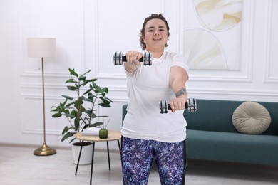 Plus size woman with dumbbells training at home