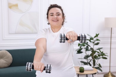 Plus size woman with dumbbells training at home