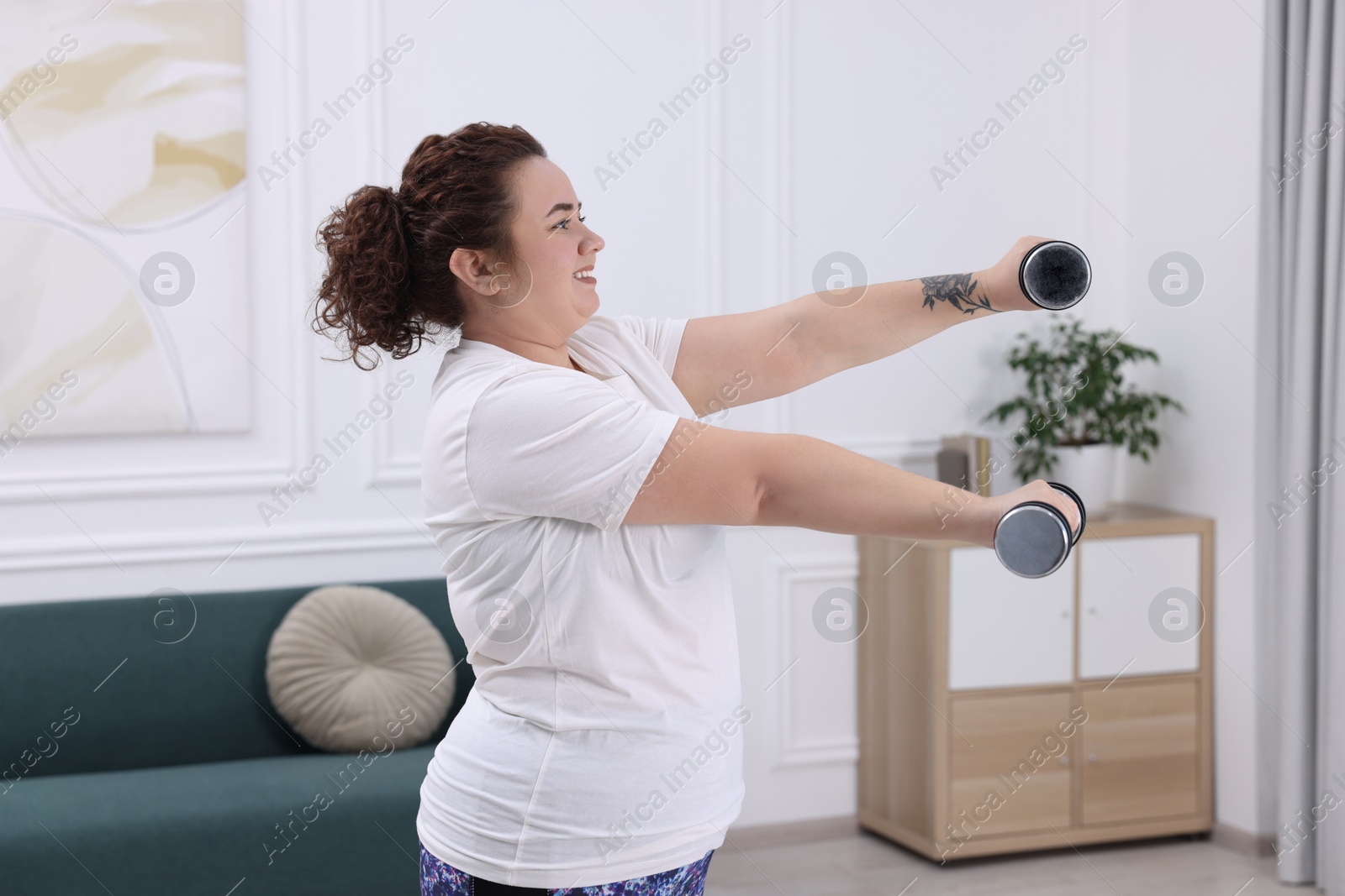 Photo of Plus size woman with dumbbells training at home