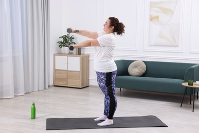 Photo of Plus size woman with dumbbells training at home