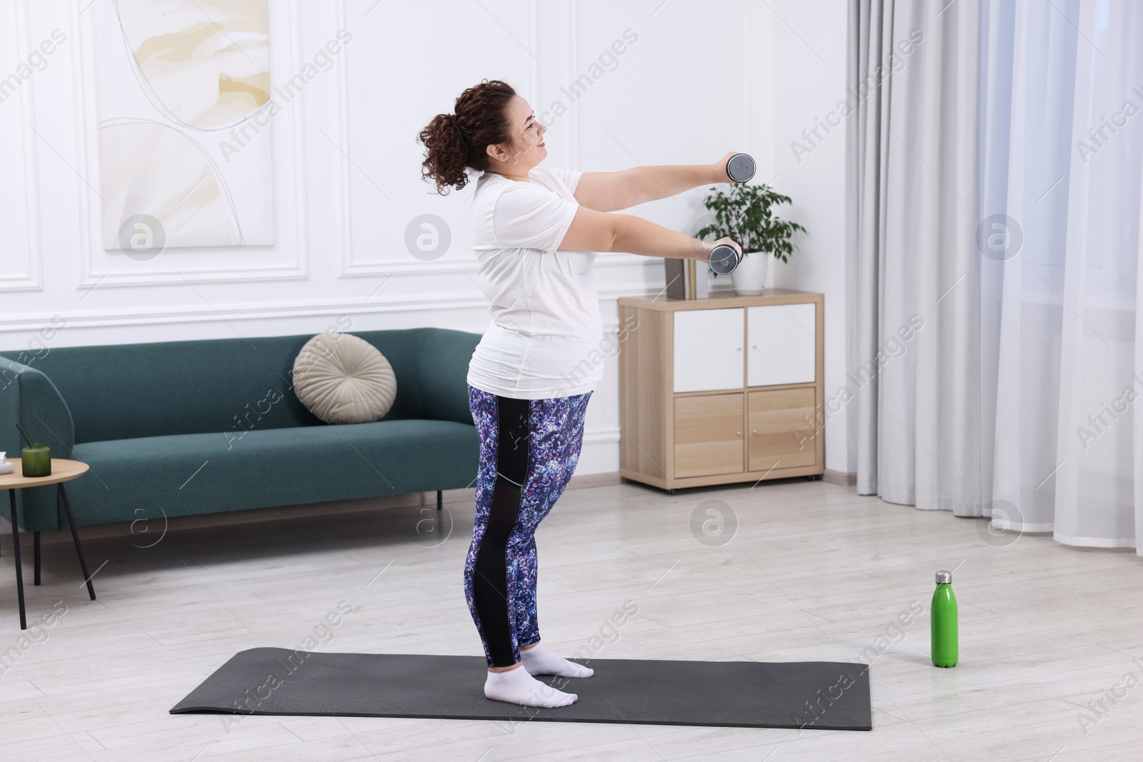 Photo of Plus size woman with dumbbells training at home