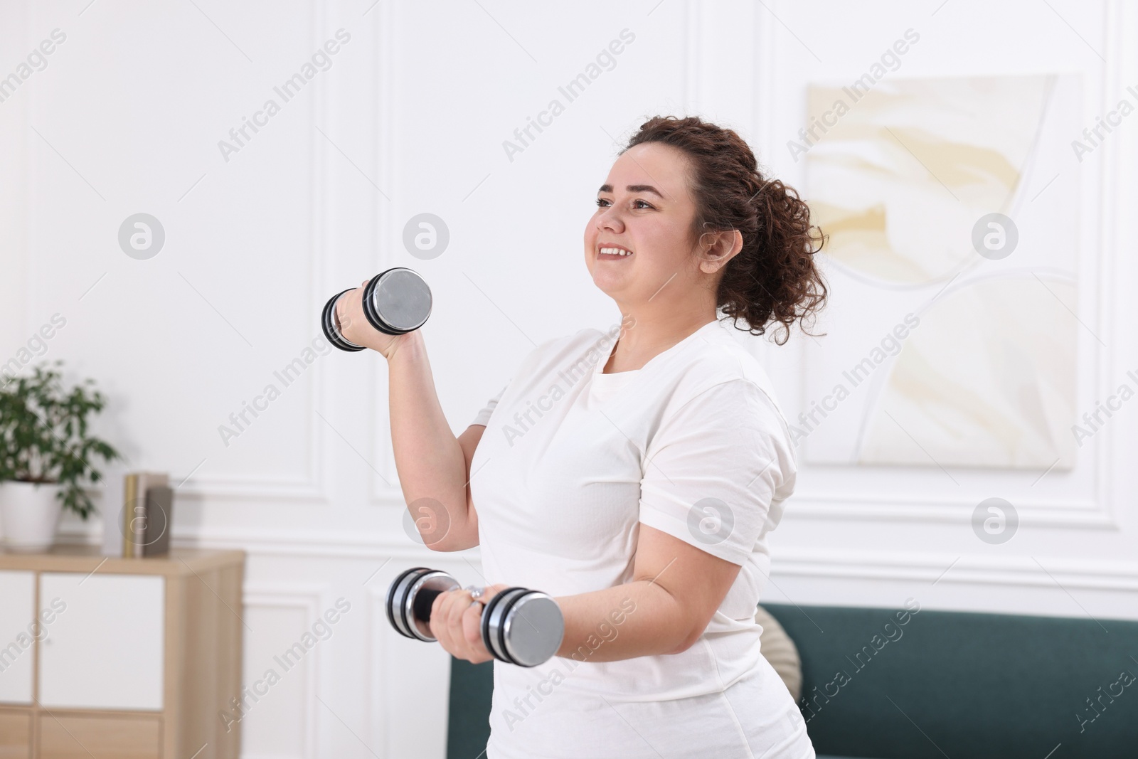 Photo of Plus size woman with dumbbells training at home