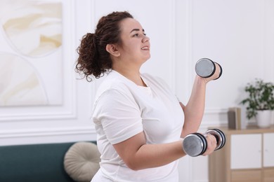 Photo of Plus size woman with dumbbells training at home