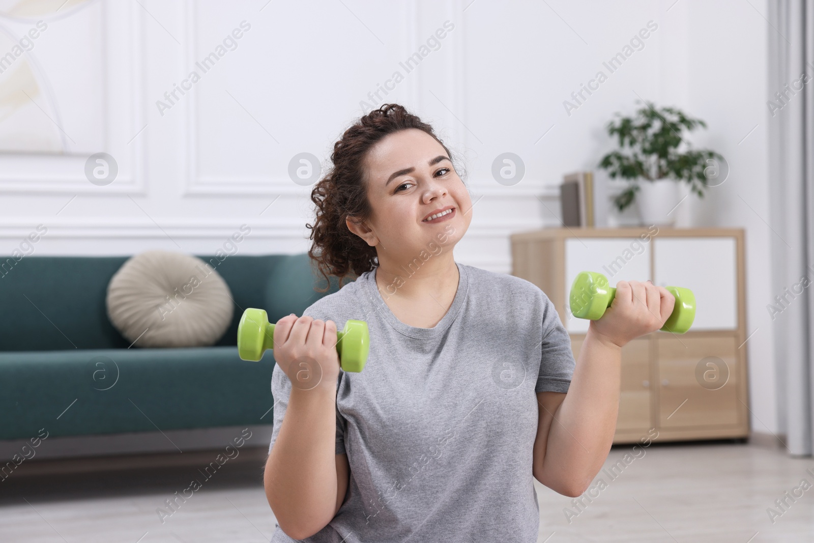 Photo of Plus size woman with dumbbells training at home