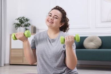 Photo of Plus size woman with dumbbells training at home