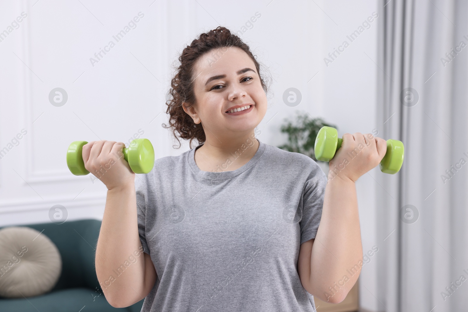 Photo of Plus size woman with dumbbells training at home